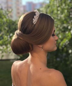 a woman with her hair in a low bun wearing a tiara and diamond earrings