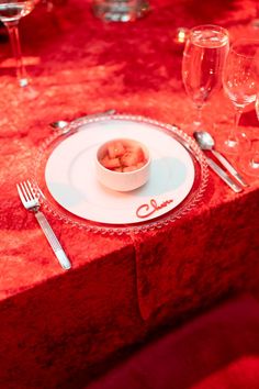 a white plate topped with food on top of a red table cloth covered table next to wine glasses