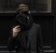 a man in a black suit and hat with his hands on his face looking down