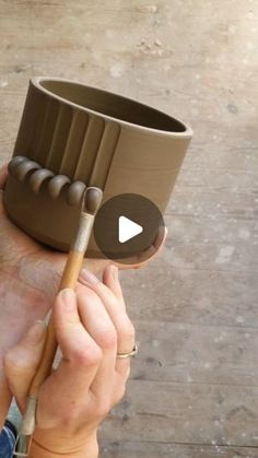 a person is holding up a clay bowl with a wooden stick in it and a video playing on the screen