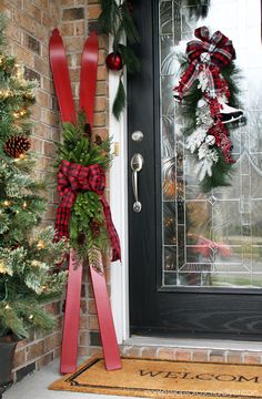 two christmas wreaths on the front door with red and green ribbons hanging from them