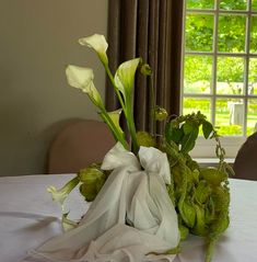 a bouquet of flowers sitting on top of a white table cloth covered table with windows in the background