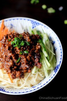 a white and blue plate topped with noodles, meat and veggies next to carrots