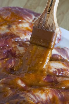 a wooden spatula being dipped with sauce on top of some meat in a white bowl