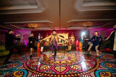 a group of people dancing on a colorful floor in a room with lights and chandeliers