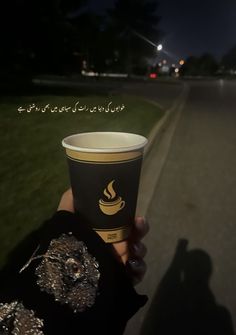 a person holding up a cup of coffee in their hand on the street at night