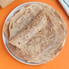 two tortillas on a white plate next to a knife and fork with an orange background