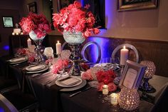 the table is set with silverware and red flowers in vases on top of it