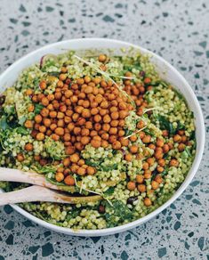 a white bowl filled with lots of food and two wooden spoons next to it