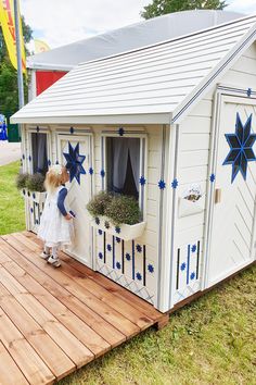 The girl looks in through the window of the wooden playhouse Cornflower by WholeWoodPlayhouses