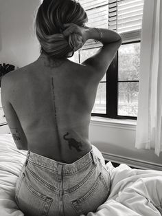 a woman sitting on top of a bed with her back turned to the camera and tattoos