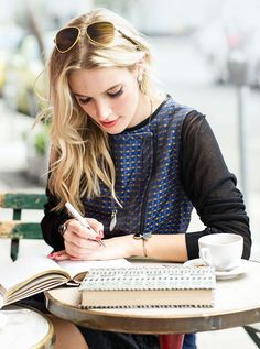 a woman sitting at a table with a book and pen in her hand while writing