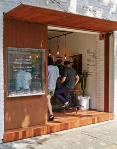 two men are standing in the open door of a small coffee shop that is decorated with wood planks