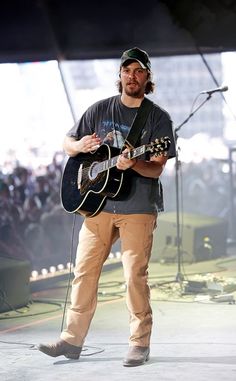 a man holding a guitar while standing in front of a microphone