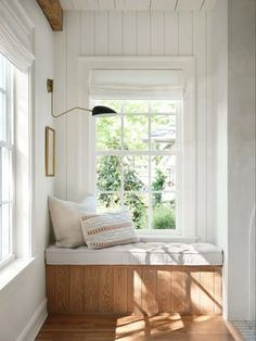 a window seat in the corner of a room with white walls and wood flooring