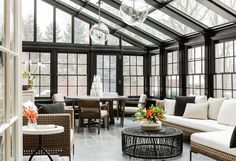 a living room filled with lots of furniture next to tall glass windows on the ceiling