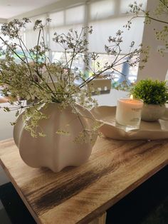 a white vase filled with flowers sitting on top of a wooden table next to a candle