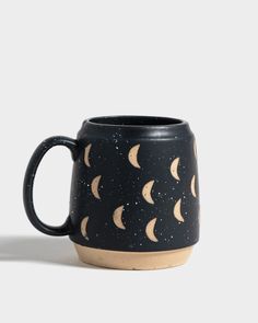 a black coffee mug with the moon phases painted on it's side, sitting in front of a white background