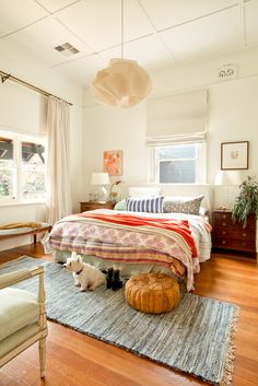 a bed room with a neatly made bed and two small dogs on the rugs