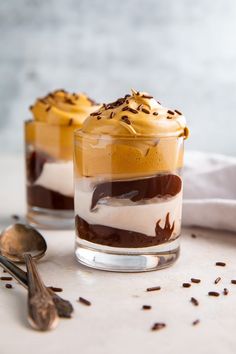 two desserts sitting on top of a white table with spoons and napkin next to them