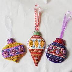 three ornaments are hanging on a white sheet and one is decorated in bright colors, the other has an ornament