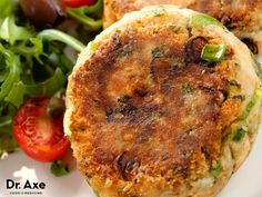 two crab cakes on a white plate next to a salad with tomatoes and lettuce