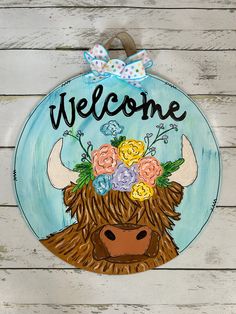 a wooden sign that says welcome with a cow's head and flowers on it