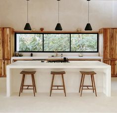 a kitchen with two stools next to an island counter and windows that look out onto the woods