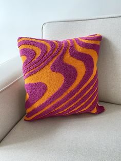 an orange and purple pillow sitting on top of a white couch next to a wall