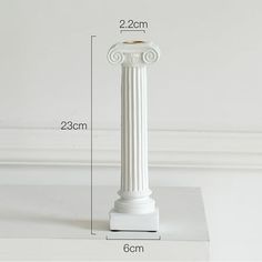 a white pedestal with a candle on top and measurements for the base, shown in front of a white wall