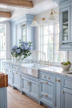 a kitchen with blue cabinets and marble counter tops, gold pulls on the handles, an island style sink and two vases filled with flowers