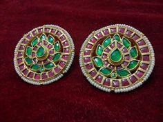 two green and pink earrings sitting on top of a red velvet covered table next to each other