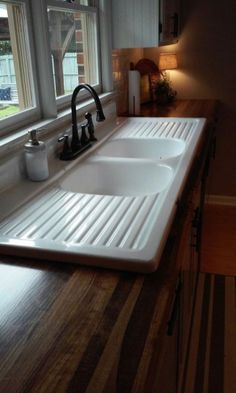 a kitchen sink sitting under a window in front of a counter top with two faucets