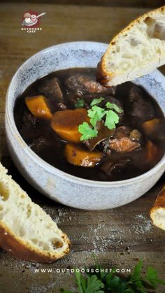 a bowl filled with stew and bread on top of a wooden table