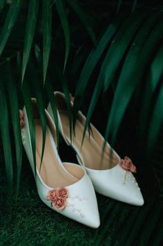 white wedding shoes with pink flowers on them sitting in front of green leaves and grass