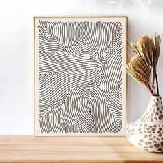 a white vase with some dry grass in it next to a framed art print on a wall