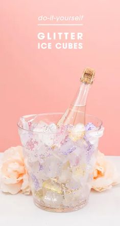 a bottle of glitter ice cubes sitting in a glass cup with flowers around it