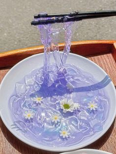 a white plate topped with water and flowers on top of a wooden table next to a bowl