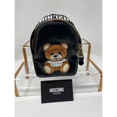 Moschino Mini Teddy Bear Embroidered Branded Backpack Black With Gold Hardware Ss21 The Teddy Bear Embroidered Branded Backpack From Moschino Features A Black Embroidered Signature Moschino Teddy Bear , Mischino Logo Embroidered At The Top, Top Zip Fastening, Single Rounded Top Handle, Main Compartment. Perfect For A Casual Day Out In The City, Festivals & Can Easily Be Styled Up Or Down. If You’re A Moschino Person ! You’ll Definitely Love This As The Gold Hardware Adds An Extra Luxurious Chic Black Leather Shoulder Bag With Embroidered Logo, Black Leather Bag With Embroidered Logo, Luxury School Bags With Logo, Moschino Teddy Bear, Mini Teddy Bears, Moschino Bags, Top Top, Top Round, Love Moschino