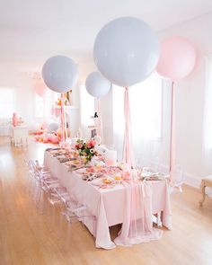 a table set up for a party with pink and white balloons in the air above it