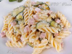 pasta with ham and zucchini on a white plate next to basil sprigs