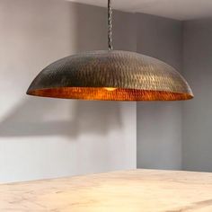 a large metal light hanging from a ceiling in a room with a wooden table and white walls