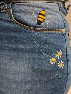 the back pocket of a pair of jeans with embroidered bees and daisies