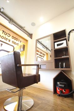 a salon chair sitting in front of a wall mounted mirror and shelf with scissors on it