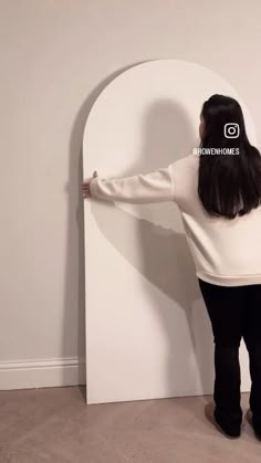 a woman standing in front of a wall with her hands on the back of it