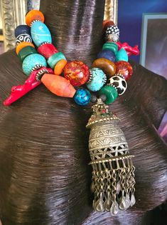 Here's a wild and exotic, OOAK Artisan Tribal Statement Necklace - Statement Pendant for those of you who like your accessories untamed! Adjusting from 16-19", this piece features a vintage metal tassel pendant with dangles, Krobo, magnesite, resin, agate, wood, zebu bone*, branch coral, chrysocolla, and assorted metals. A bold, chunky and heavy piece, this closes with a fancy silver tone tribal hook and a 3" silver tone extender chain. The pendant measures 5" x 2" and has inlaid glass. A perfec Bohemian Beaded Necklaces With Large Beads For Festive Occasions, Bohemian Festive Beaded Necklace With Large Beads, Eclectic Handmade Beaded Necklaces For Festivals, Bohemian Jewelry With Large Beads For Festivals, Festival Multicolor Bohemian Beaded Necklaces, Bohemian Large Beads Jewelry For Festival, Adjustable Bohemian Beaded Necklaces For Festive Occasions, Bohemian Beaded Necklaces For Festive Occasions, Bohemian Beaded Necklace For Festive Occasions