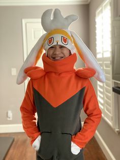 a young boy in an orange and black costume with a bird on his head, smiling at the camera