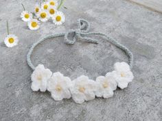 white crocheted flowers are tied to a gray string on the ground next to daisies