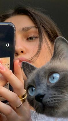 a woman looking at her cell phone with a cat on her shoulder next to her