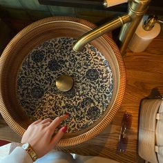 a woman's hand is on the edge of a decorative bowl that sits on a table